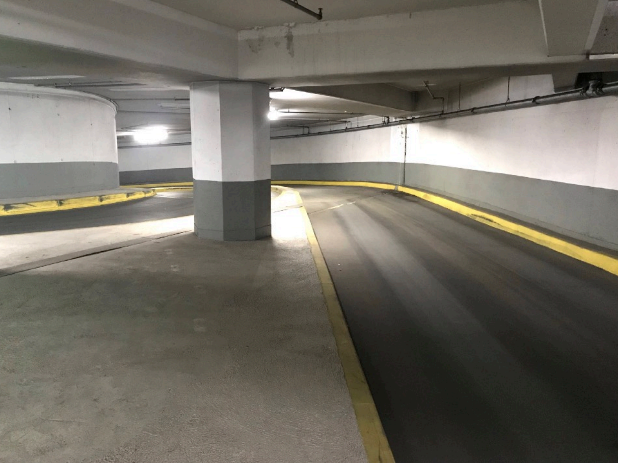 Leere Parkhausrampe mit mittiger Säule, kurviger Fahrbahn und gelben Bordkanten.